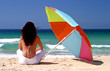 woman sitting under colorful parasol on white sandy beach
