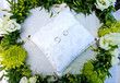 wedding rings on a white cushion in a wreath of flowers