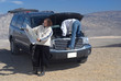 a woman tries to fix a car while husband reads a map