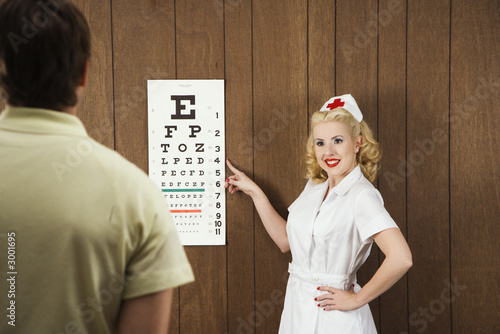 Photo: female nurse pointing out eye chart to man. female nurse pointing out eye chart to man.