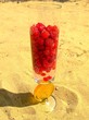 Glass of mineral water and fruit standing on beach sand
