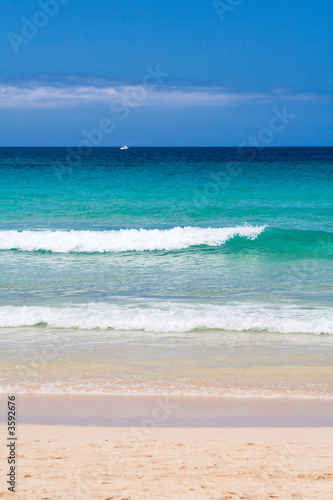 wellen am strand von corralejo, fuerteventura, weisses boot