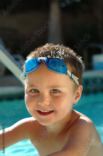 Smiling young kid in swimming goggles standing waist-high