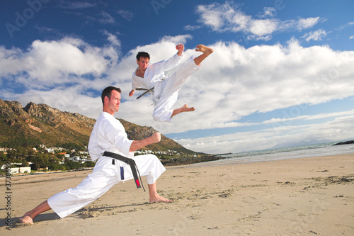 Foto: Young adult men with black belt practicing on the beach Young adult men with black belt practicing on the beach