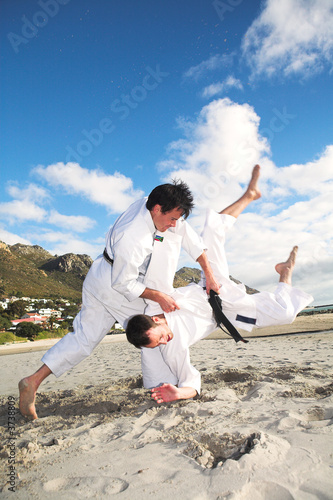 Photo: Men with black belt practicing fighting on the beach Men with black belt practicing fighting on the beach