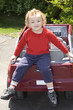 Young blond with curly hair sitting on tailgate of car