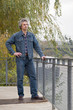 Middleaged man in a jean suit stands on a river bank