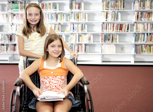 Photo: Two school girls at the library. One is in a wheelchair. Two school girls at the library. One is in a wheelchair.