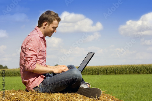 Photo: handosme man with laptop over country view. handosme man with laptop over country view.