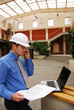 contractor in hardhat calling by phone and work with laptop