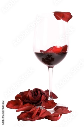 Photo: Glass on red wine with a rose and rose petals isolated on white Glass on red wine with a rose and rose petals isolated on white