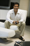Photo: Man with remote control sitting in front of Large Screen TV in living room, portrait Man with remote control sitting in front of Large Screen TV in living room, portrait