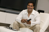 Photo: Man with remote control sitting in front of Large Screen TV in living room, portrait Man with remote control sitting in front of Large Screen TV in living room, portrait