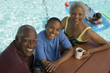 Boy 13-15 sitting with grandparents at picnic table by swimming pool, elevated view portrait.