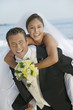 Groom giving Bride piggyback ride, outdoors, portrait