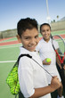 Young boy and girl with tennis equipment on tennis court, focus on boy, portrait