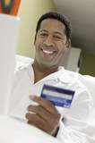 Photo: Man on sofa Using Credit Card to Make Purchase with Laptop, portrait, low angle view Man on sofa Using Credit Card to Make Purchase with Laptop, portrait, low angle view