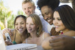 Foto: Group of friends at back yard table using laptop and cell phone, close up Group of friends at back yard table using laptop and cell phone, close up
