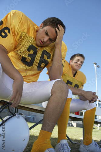 Photo: Two football players sitting on bench, low angle view Two football players sitting on bench, low angle view
