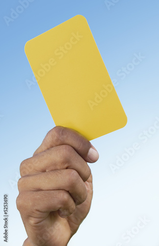 Photo: Soccer referee holding up yellow card, close-up on hand Soccer referee holding up yellow card, close-up on hand