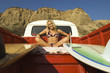 Young woman in bikini sitting with surfboards in back of truck, low angle view