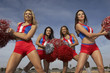 Cheerleaders doing routine with pom poms on football field
