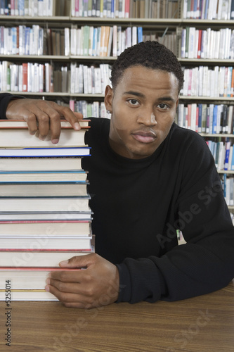Foto: Male student with a stack of books in library Male student with a stack of books in library