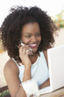 Woman using mobile phone while sitting in front of laptop, portrait