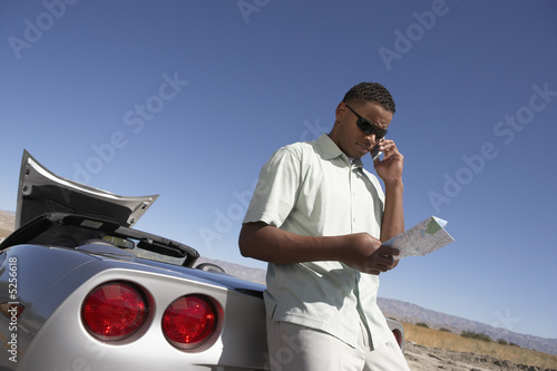 Foto: Man using cell phone and map by sports car at side of road Man using cell phone and map by sports car at side of road
