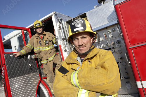 Photo: Two fire fighters standing by fire engine Two fire fighters standing by fire engine