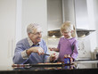 Girl 3-4 and grandfather spreading jam on biscuits in kitchen