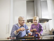 Girl 3-4 and grandfather spreading jam on biscuits in kitchen