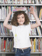 Girl balancing stack of books on head in library, portrait