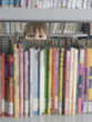 Boy peeking from behind bookshelf in library