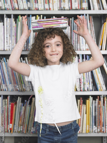 Girl balancing stack of books on head in library, portrait