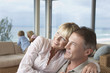 Wife sitting on husband's lap, arms around, on vacation near seaside with children