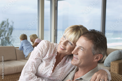 Photo: Wife sitting on husband's lap, arms around, on vacation near seaside with children Wife sitting on husband's lap, arms around, on vacation near seaside with children