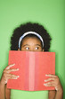 girl with book held up to face looking suspiciously to the side.