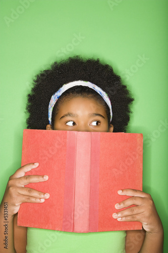 Foto: girl with book held up to face looking suspiciously to the side. girl with book held up to face looking suspiciously to the side.