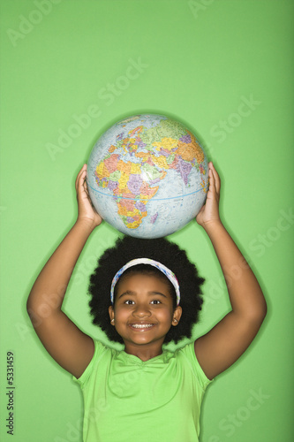 Photo: Girl holding globe on top of head and smiling at viewer. Girl holding globe on top of head and smiling at viewer.