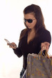 Young girl holding bags and sending message on mobile