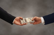 Two hands of businessmen passing a stack of dollars