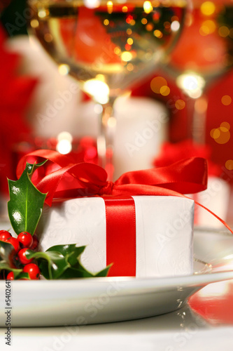 Little red ribboned gift with a sprig of holly on plate