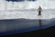 Young man's walking in the sea, on a black sand beach
