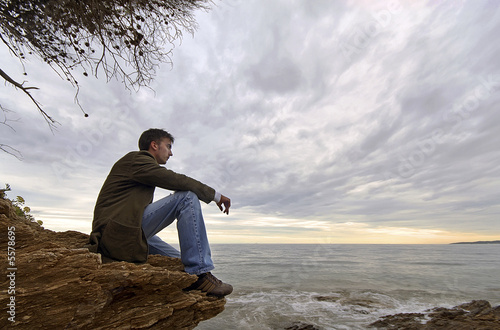 Photo : jeune homme assis seul face à la mer solitude tristesse jeune homme assis seul face à la mer solitude tristesse