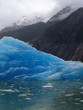Blue iceberg under mountain clouds