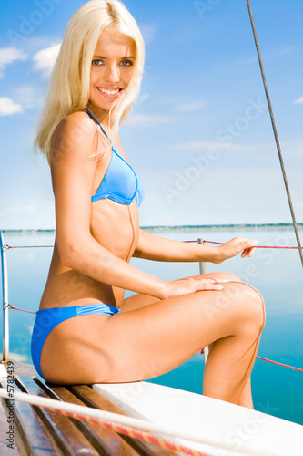 Blonde girl sitting on a bench on the background of sky and lake