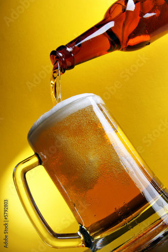 Foto: Pouring beer into mug over yellow background Pouring beer into mug over yellow background