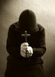 A monk praying with a rosary and crucifix in his hand.