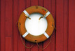 Orange lifebelt and lifeline on red wooden wall